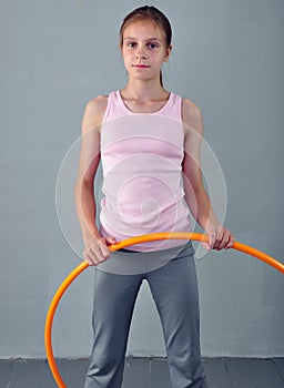 Teenage sportive girl is doing exercises with hula hoop to develop muscle on grey background. Having fun playing game hula-hoop.