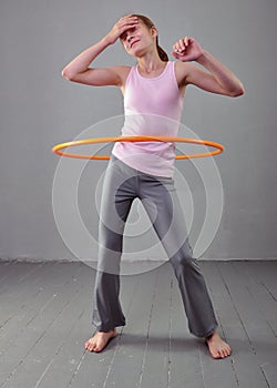 Teenage sportive girl is doing exercises with hula hoop to develop muscle on grey background. Having fun playing game . Sport heal