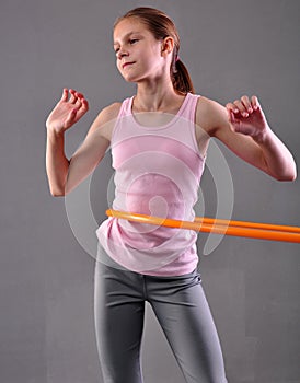 Teenage sportive girl is doing exercises with hula hoop to develop muscle on grey background. Having fun playing game . Sport heal