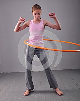 Teenage sportive girl is doing exercises with hula hoop to develop muscle on grey background. Having fun playing game . Sport heal