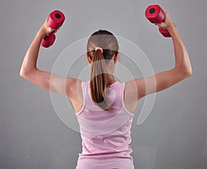 Teenage sportive girl is doing exercises to develop with dumbbells muscles on grey background. Sport healthy lifestyle concept. Sp