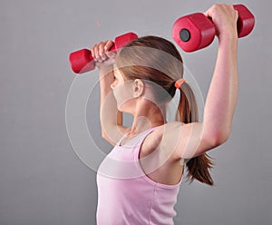 Teenage sportive girl is doing exercises to develop muscles on grey background. Sport healthy lifestyle concept. Sporty