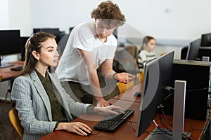 Teenage student talking to female teacher sitting at computer in class