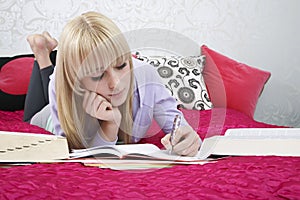 Teenage Student Writing In Book On Bed