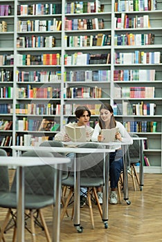 teenage students reading books near bookshelves