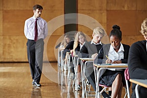 Teenage Students Sitting Examination With Teacher Invigilating