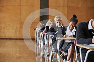 Teenage Students In Uniform Sitting Examination In School Hall