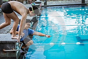teenage swimmer standing on block board and preparing to jump and swim with a coach giving instructions