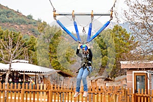 Teenage teen girl bungee flying in rope amusement park. Climbing harness equipment, green sports safety helmet