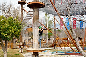 Teenage teen girl in climbing harness equipment, green sports safety helmet. Rope amusement park. Fastening