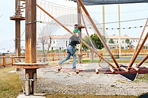 Teenage teen girl in climbing harness equipment, green sports safety helmet. Rope amusement park. Fastening