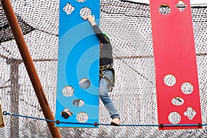 Teenage teen girl in climbing harness equipment, green sports safety helmet. Rope amusement park. Fastening