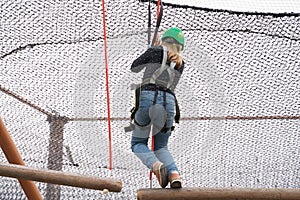 Teenage teen girl in climbing harness equipment, green sports safety helmet. Rope amusement park. Fastening