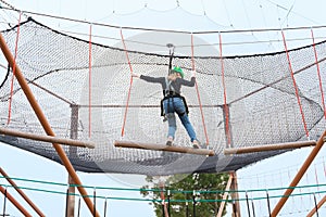 Teenage teen girl in climbing harness equipment, green sports safety helmet. Rope amusement park. Fastening