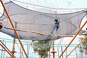 Teenage teen girl in climbing harness equipment, green sports safety helmet. Rope amusement park. Fastening