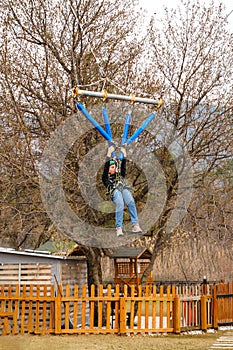 Teenage teen girl in climbing harness equipment, green sports safety helmet. Rope amusement park. Fastening