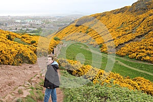 Teenage woman smiles happily while walking along the mountain that is full of yellow flowers