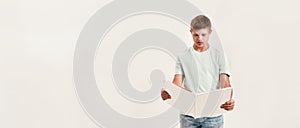 Teenaged disabled boy with Down syndrome looking focused while reading a book, standing isolated over white background