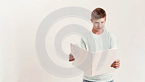 Teenaged disabled boy with Down syndrome looking focused while reading a book, standing isolated over white background