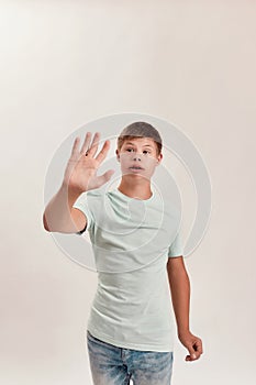 Teenaged disabled boy with Down syndrome showing stop sign with his hand while posing isolated over white background