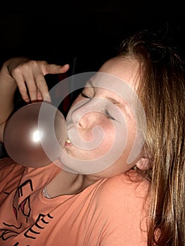 A teenagegirl making a balloon with chewing gum in a dark room