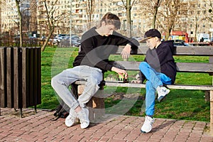 Teenager and an 8-year-old boy, are sitting on park bench playing chess.