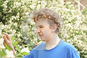 Teenager with allergies standing in a blue t-shirt among the Jasmine bushes and suffers from bad health