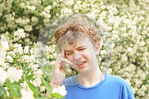 Teenager with allergies standing in a blue t-shirt among the Jasmine bushes and suffers from bad health