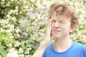 Teenager with allergies standing in a blue t-shirt among the Jasmine bushes and suffers from bad health