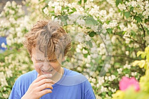 Teenager with allergies standing in a blue t-shirt among the Jasmine bushes and suffers from bad health