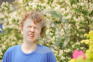 Teenager with allergies standing in a blue t-shirt among the Jasmine bushes and suffers from bad health