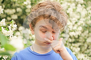 Teenager with allergies standing in a blue t-shirt among the Jasmine bushes and suffers from bad health