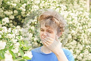 Teenager with allergies standing in a blue t-shirt among the Jasmine bushes and suffers from bad health