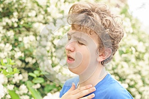 Teenager with allergies standing in a blue t-shirt among the Jasmine bushes and suffers from bad health