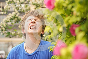 Teenager with allergies standing in a blue t-shirt among the Jasmine bushes and suffers from bad health