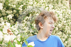 Teenager with allergies standing in a blue t-shirt among the Jasmine bushes and suffers from bad health