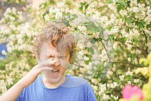 Teenager with allergies standing in a blue t-shirt among the Jasmine bushes and suffers from bad health