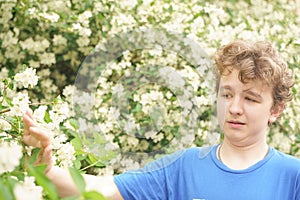 Teenager with allergies standing in a blue t-shirt among the Jasmine bushes and suffers from bad health