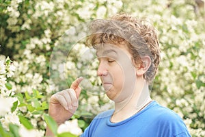 Teenager with allergies standing in a blue t-shirt among the Jasmine bushes and suffers from bad health