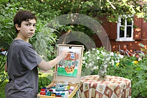 Teenager artist boy in garden painting picture of jasmin flowers and cottage house