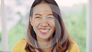 Teenager Asian woman feeling happy smiling and looking to camera while relax in her living room at home.