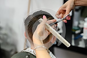 A teenager in a beauty salon gets a haircut, a hairdresser cuts a teenage boy& x27;s hair.