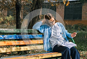 A teenager on a bench is doing homework on a sunny autumn day.