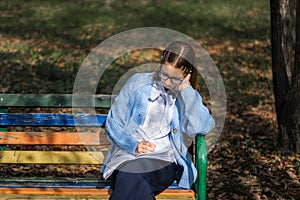 A teenager on a bench is doing homework on a sunny autumn day.
