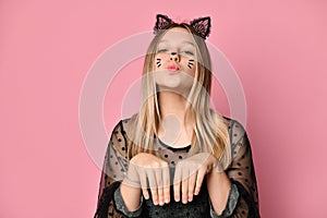 Adolescent in black dress, headband like cat ears, face painting. She posing on pink background. Close up