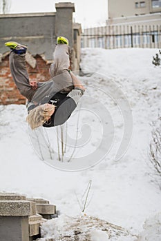 Teenager blonde hair guy training parkour jump flip in the snow covered park photo