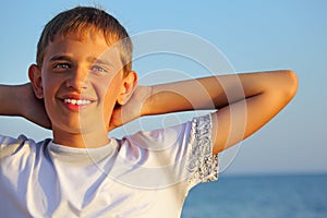 Teenager boy against sea, hands behind head