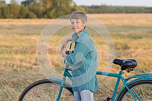 Teenager boy with bicycle in sunset farm field