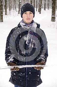 Teenager boy in a blue jacket, in a checkered scarf and in a dark blue hat with a icicle in his hands