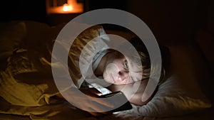 Teenager boy chatting by phone, writing in blog or reading social networks instead sleeping. Young guy laying in bed and watching